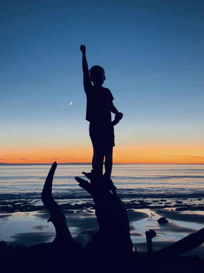 Child raising a fist at the beach at sunset.
